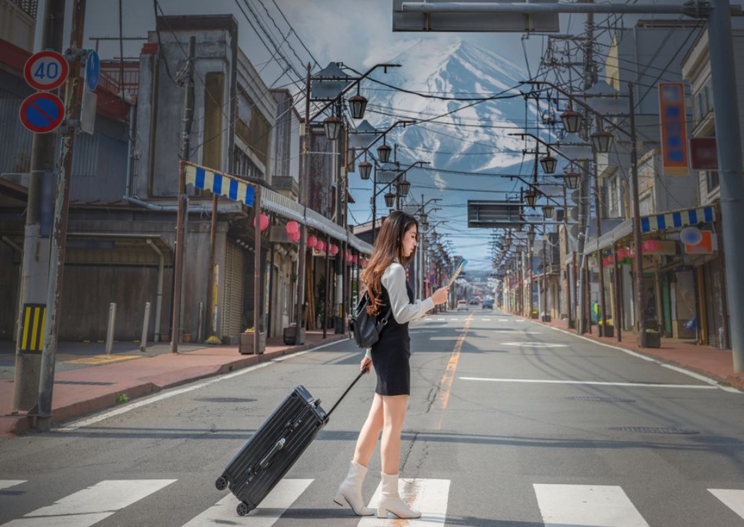 Donna con I propri bagagli che tiene in mano una mappa su una strada Fujiyoshida con il Monte Fuji sullo sfondo.