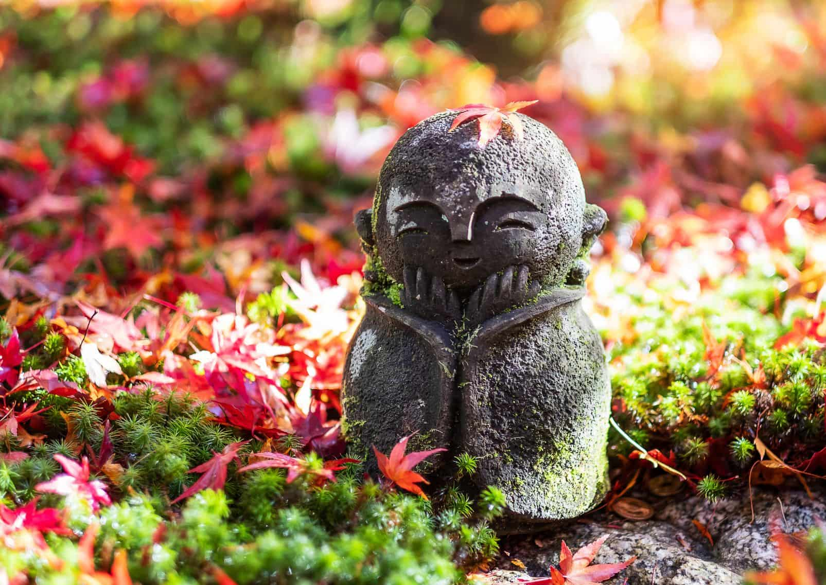 bambola giapponese Jizo con una foglia d'acero rossa che cade nel giardino giapponese del Tempio Enkoji, Kyoto, Giappone