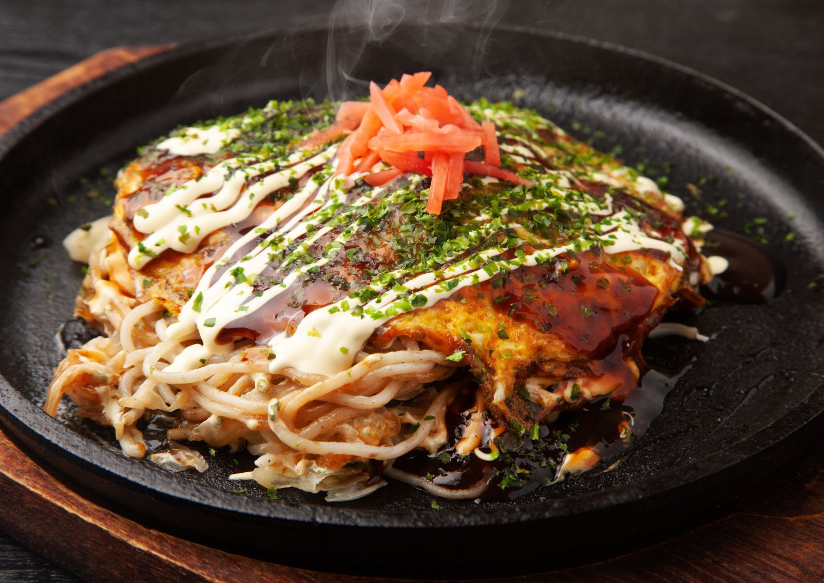 Spessa frittella okonomiyaki alla Hiroshima ripiena di noodle e condita con salse