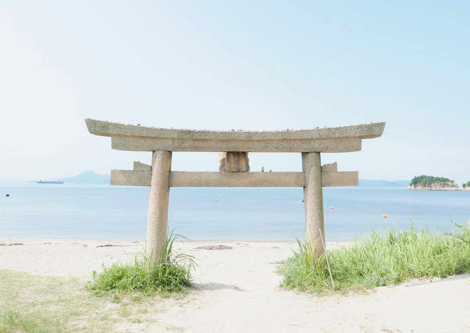 Un torii in pietra semisommerso nella sabbia con il mare sullo sfondo