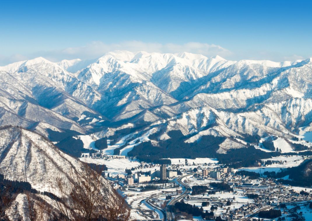 Vista panoramica di una località sciistica giapponese circondata da montagne innevate sotto un cielo azzurro limpido.