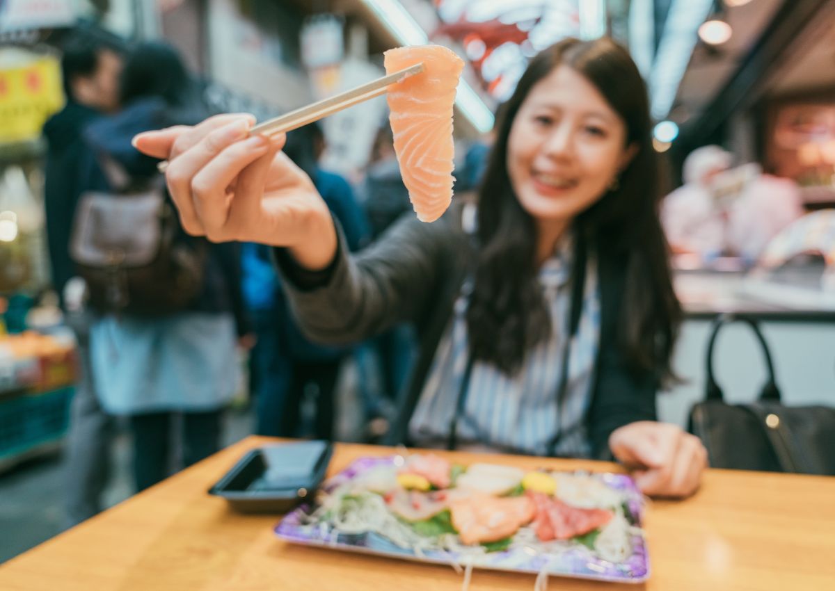Ragazza che mangia sushi al mercato di Kuromon, Osaka, Giappone