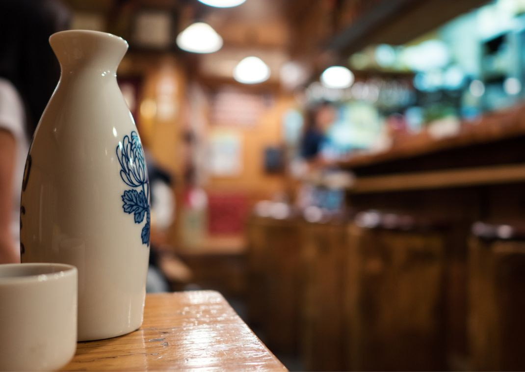 Bottiglia e tazza di sake con ristorante sfocato sullo sfondo.