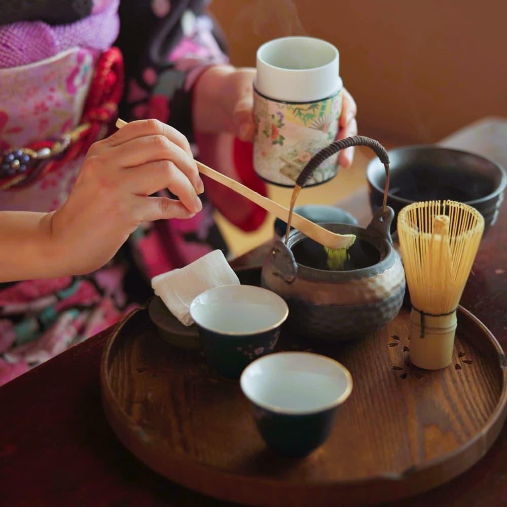 Donna giapponese che prepara il tè matcha in una tradizionale cerimonia del tè a casa, con polvere di matcha, erbe e teiera