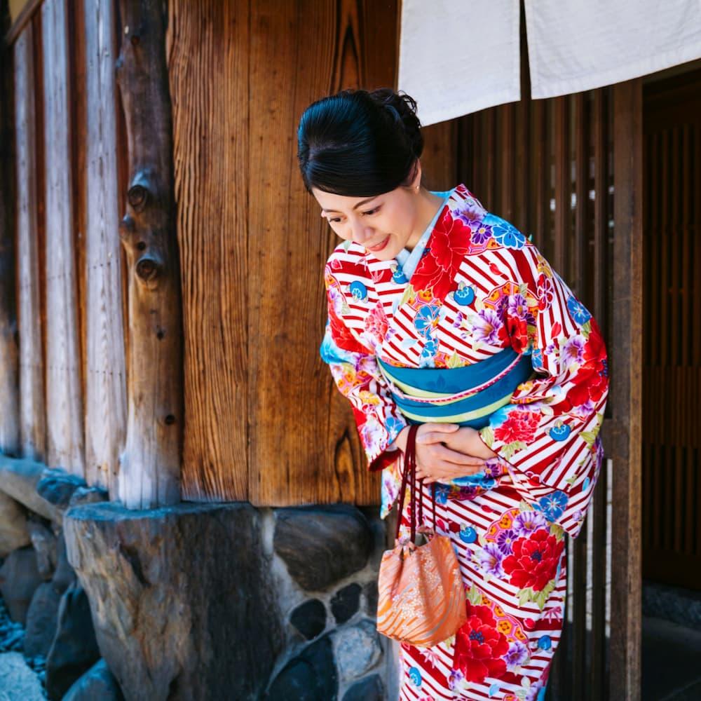 Donna giapponese con un kimono colorato che si inchina davanti a un edificio tradizionale in legno a Kyoto