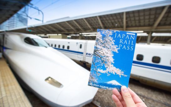 Mano che tiene un biglietto del Japan Rail Pass davanti a uno Shinkansen alla stazione di Tokyo