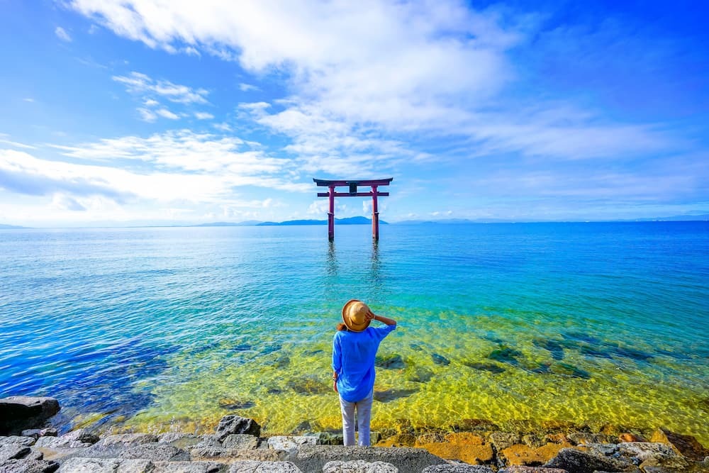 Viaggiatore in piedi vicino a un cancello torii presso il lago Biwa nella prefettura di Shiga, Giappone