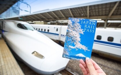 Mano che tiene un biglietto del Japan Rail Pass davanti a uno Shinkansen alla stazione di Tokyo