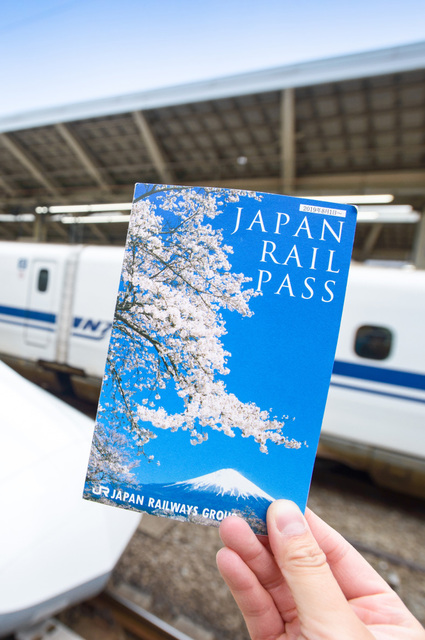 Mano che tiene un biglietto del Japan Rail Pass davanti a uno Shinkansen alla stazione di Tokyo
